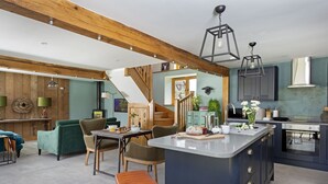 Una cocina moderna con una isla central, vigas de madera y un comedor con sofás verdes y taburetes de madera.
