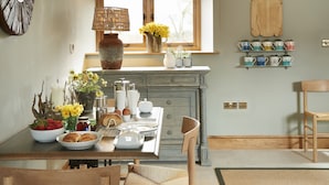 A dining area with a wooden table set for breakfast, a window with a view, and a shelf with decorative items. - The Stone Barn is a romantic and restorative barn conversion for adults (Downton-on-the-Rock)