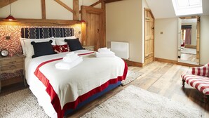 A bedroom with a large bed, wooden beams, a skylight, a nightstand, a red lamp, and a chair. - The Stone Barn is a romantic and restorative barn conversion for adults (Downton-on-the-Rock)