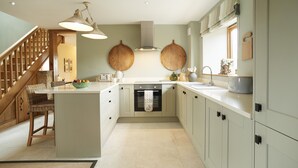 A kitchen with a central island, wooden stools, a hanging light fixture, and a built-in oven. - The Stone Barn is a romantic and restorative barn conversion for adults (Downton-on-the-Rock)