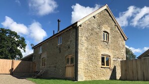 A stone building with a sloped roof, two wooden doors, and a satellite dish. - The Stone Barn is a romantic and restorative barn conversion for adults (Downton-on-the-Rock)
