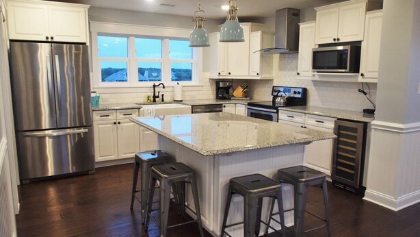 A modern kitchen with stainless steel appliances, a large island with stools, and a view of the outdoors through the window. - Ocean View - Family Friendly - Steps to Beach (Bald Head Island)