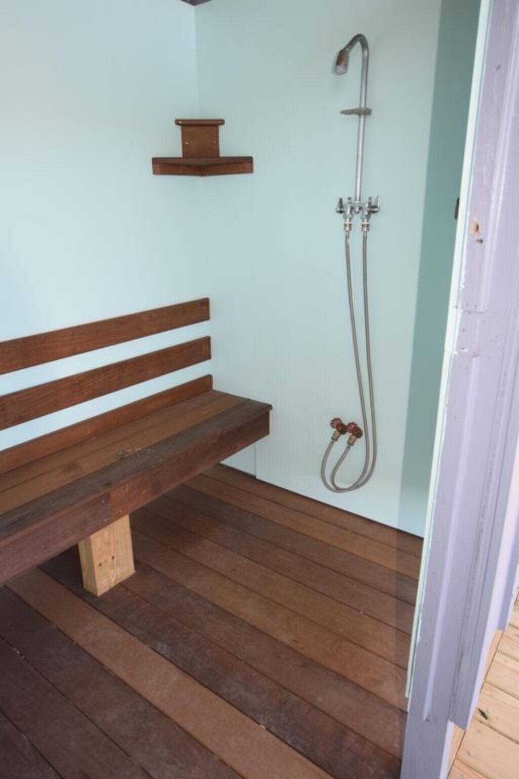 A wooden bench in a room with a shower area.