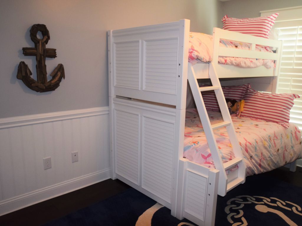 A bunk bed with a white ladder, a decorative anchor on the wall, and a patterned rug.
