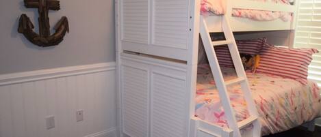 A bunk bed with a white ladder, a decorative anchor on the wall, and a patterned rug.