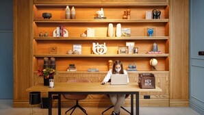 A person working at a wooden desk with a laptop, surrounded by shelves with various decorative items. - Mercure Porto Centro Aliados (Porto)
