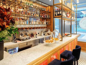 Una zona de bar con estantes llenos de botellas, una máquina de café y una exposición de pasteles.