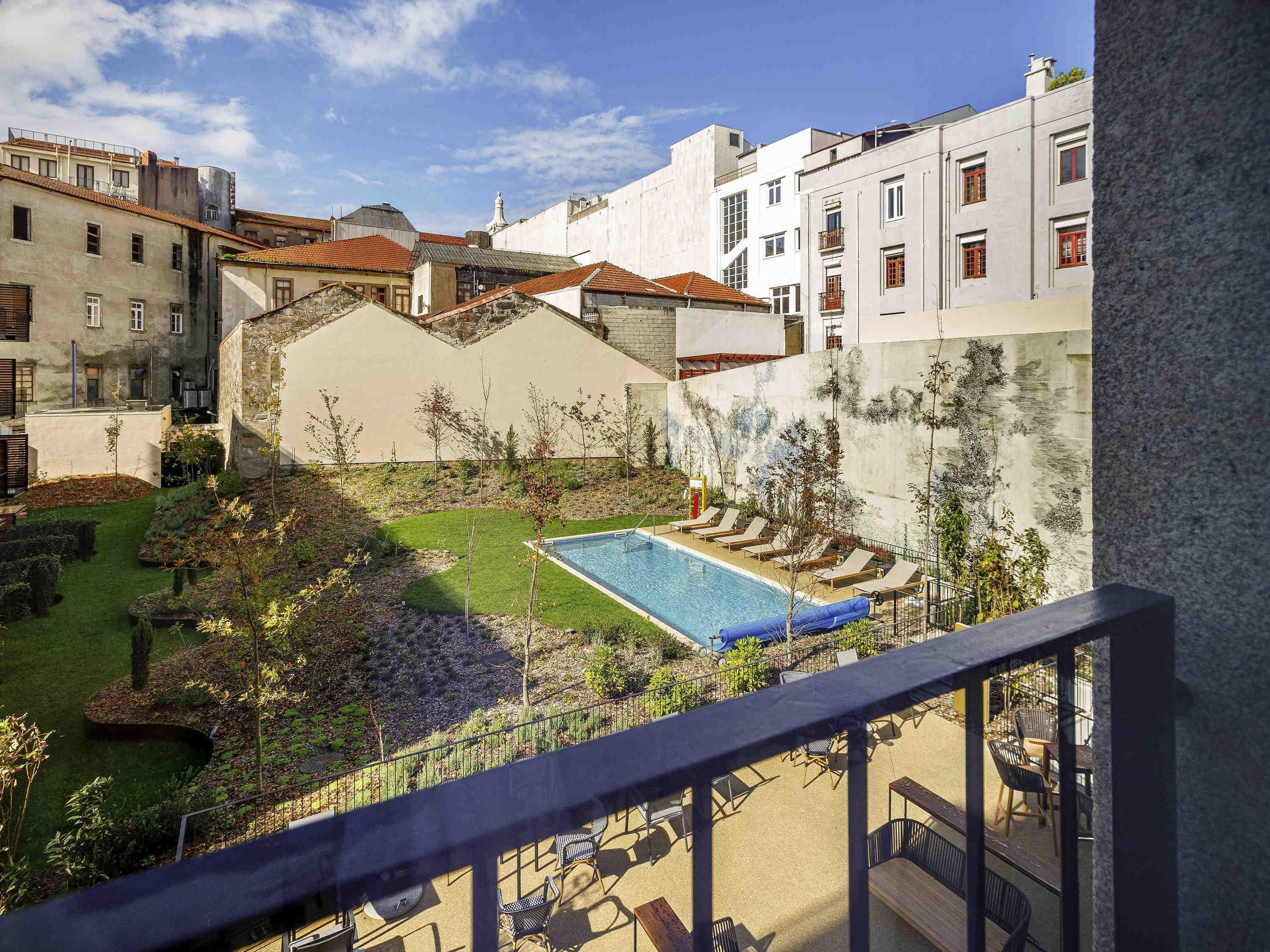 Zona de piscina con sillas de descanso, un pequeño jardín y edificios al fondo.