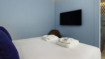A hotel room with a bed, a flat-screen TV mounted on the wall, and a chair.