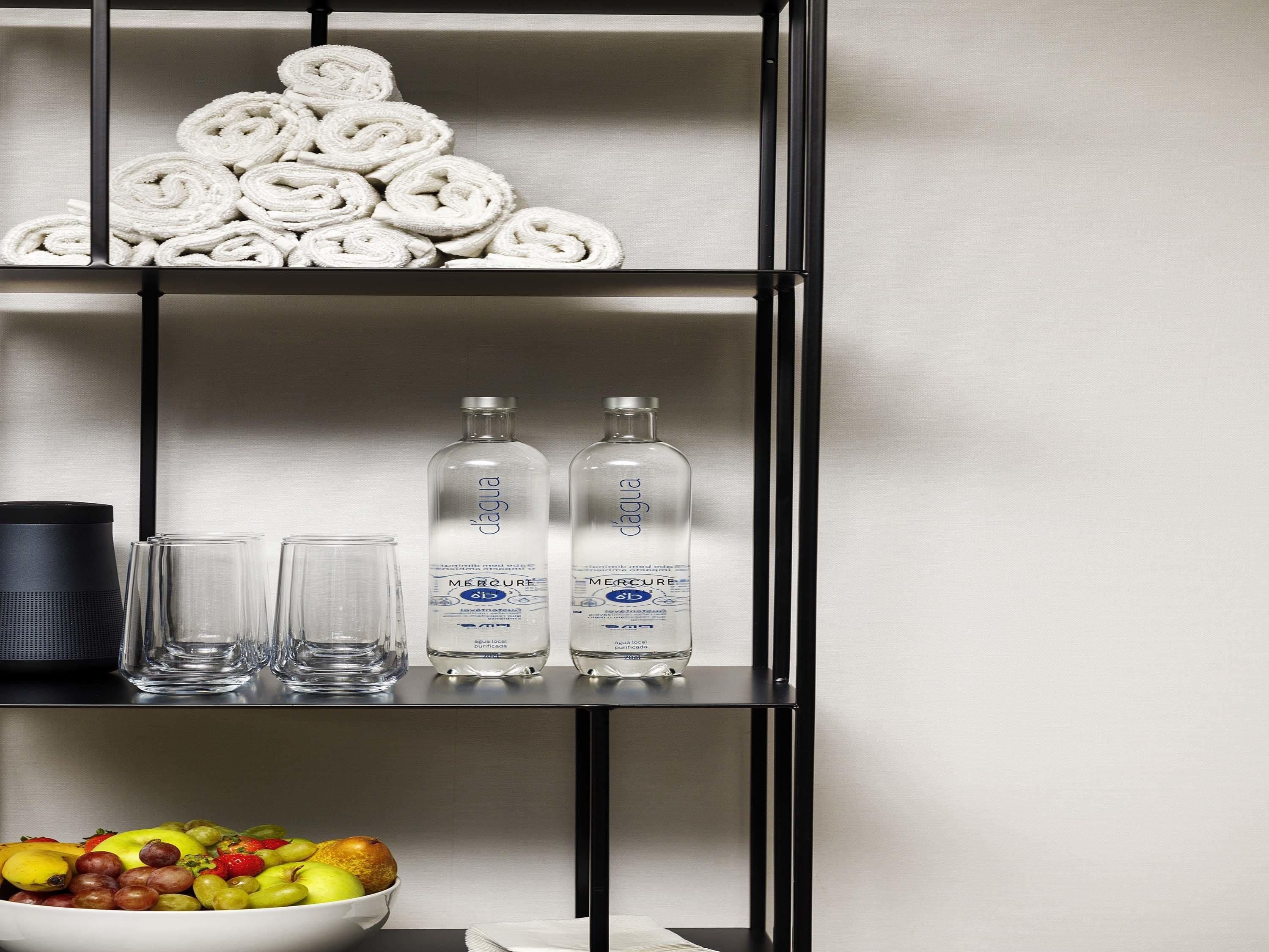 A shelf with rolled towels, two bottles of water, and a bowl of fruit.