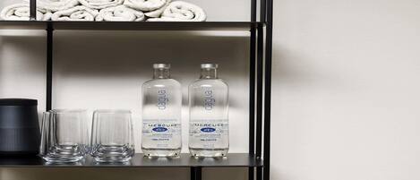 A shelf with rolled towels, two bottles of water, and a bowl of fruit.