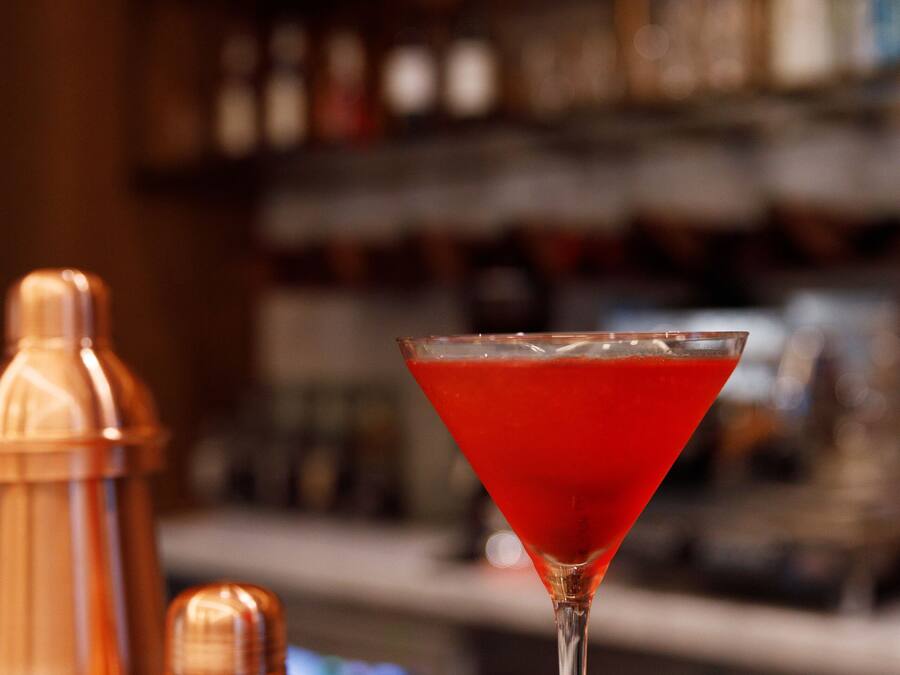Una copa de martini con un cóctel rojo sobre una barra.