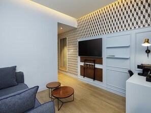 A modern living room with a sofa, two small round tables, a flat-screen TV, and a patterned wall. - Mercure Porto Centro Aliados (Porto)
