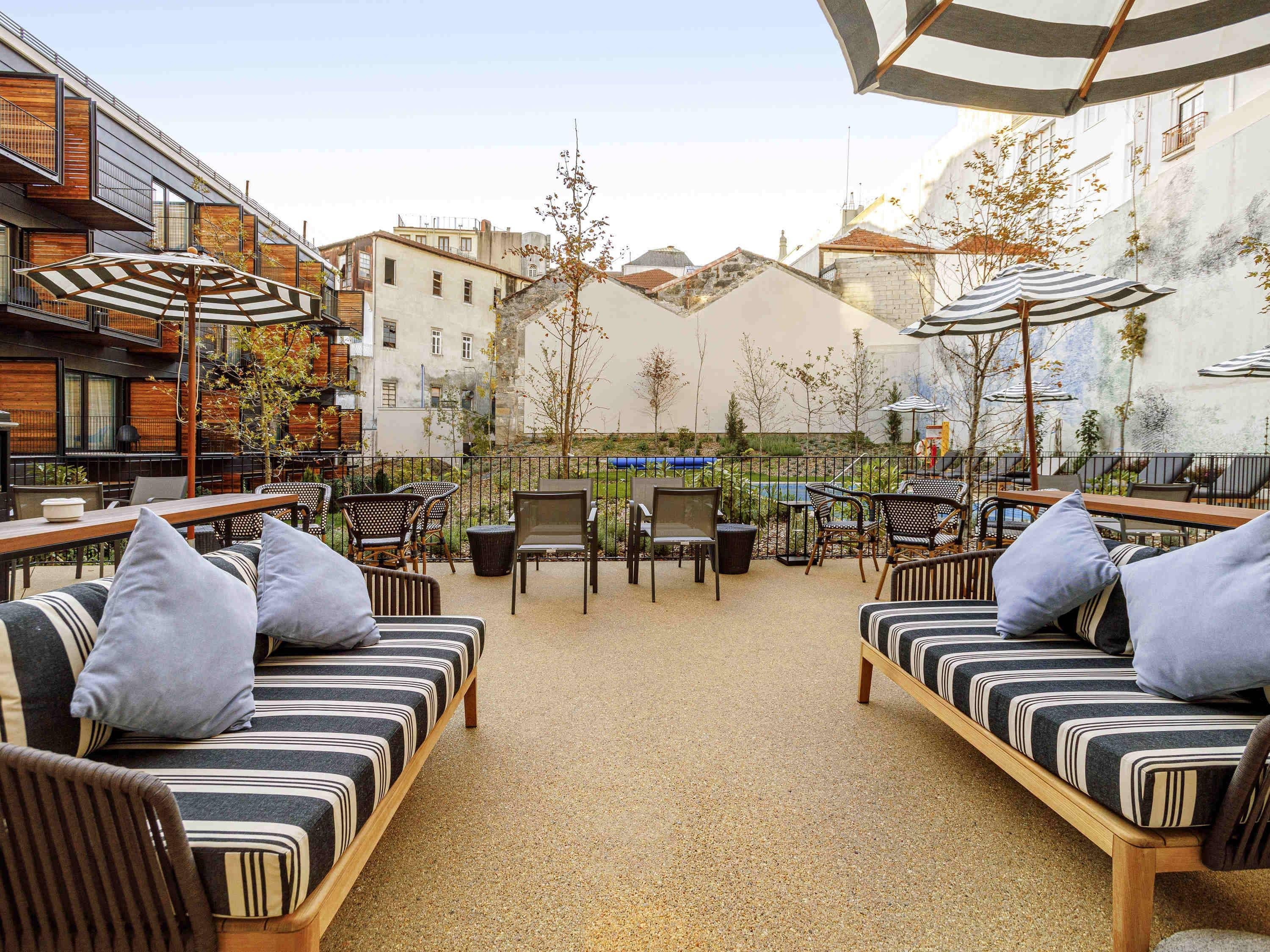 Un área de estar al aire libre con sofás y sillones, una piscina y edificios al fondo.