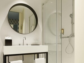 A modern bathroom with a round mirror, a white sink, a glass shower enclosure, and a black vanity. - Mercure Porto Centro Aliados (Porto)