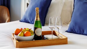A neatly made bed with a tray of fruits, a bottle of champagne, and two glasses on a hotel room.