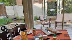 An outdoor dining area with a table set for two, featuring a bottle of iced tea, a jar of jam, a mug, and a plate with cutlery. - Au Bon Vivant (Dampierre-sur-Salon)