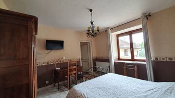 Ein Schlafzimmer mit Bett, Schreibtisch, Stuhl, Fernseher und einem Fenster mit Vorhängen.