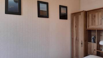 A bedroom with a bed, a wooden wardrobe, and three framed pictures on the wall.