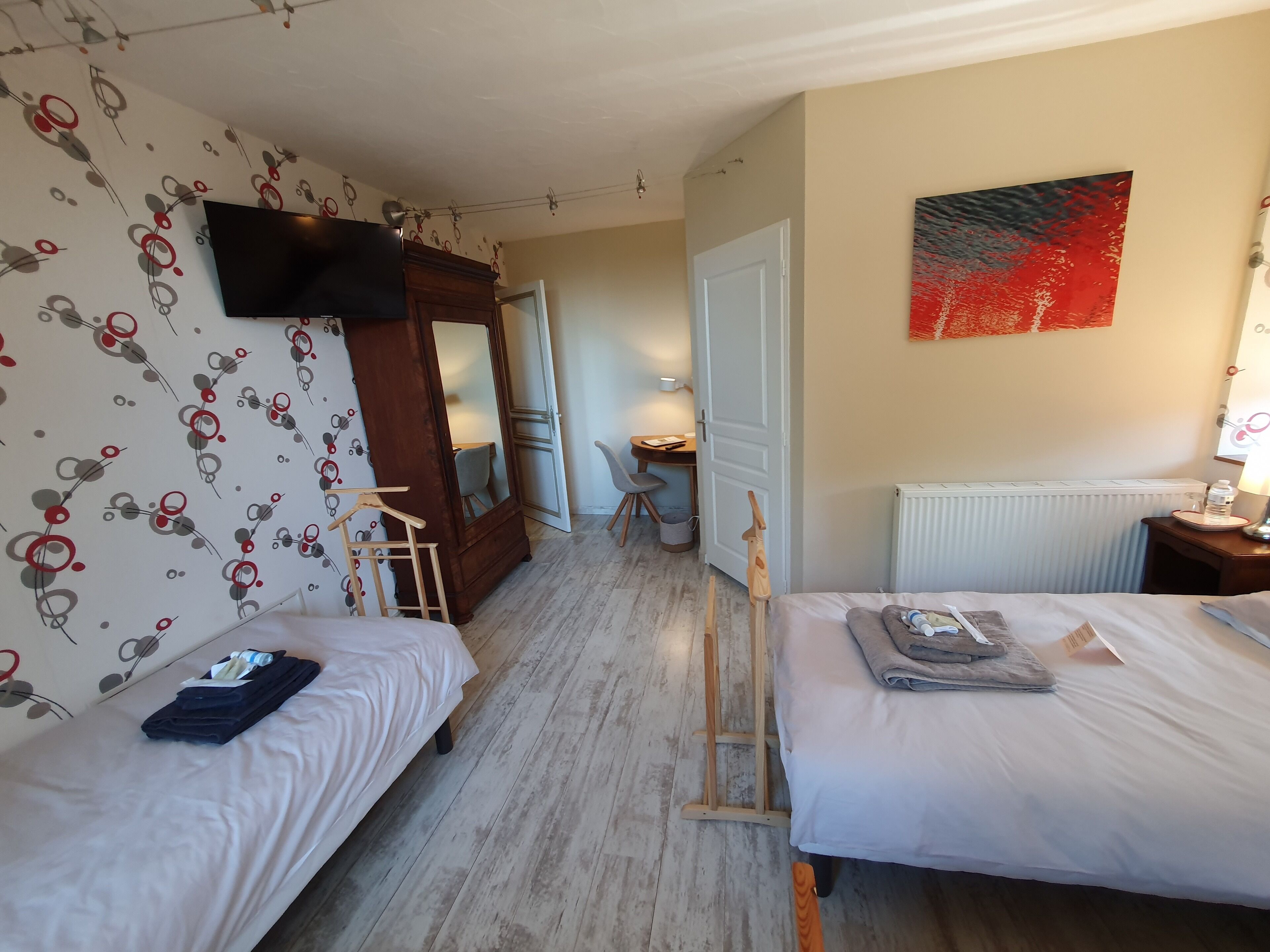 A hotel room with two beds, a TV, a painting, and a desk with a chair.