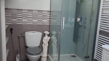 Un baño moderno con cabina de ducha de vidrio, inodoro y una estatua decorativa.