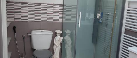 A modern bathroom with a glass shower enclosure, a toilet, and a decorative statue.