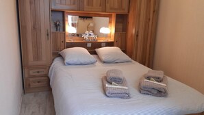 A bedroom with a bed, two pillows, a nightstand, a mirror, and wooden cabinets. - Au Bon Vivant (Dampierre-sur-Salon)