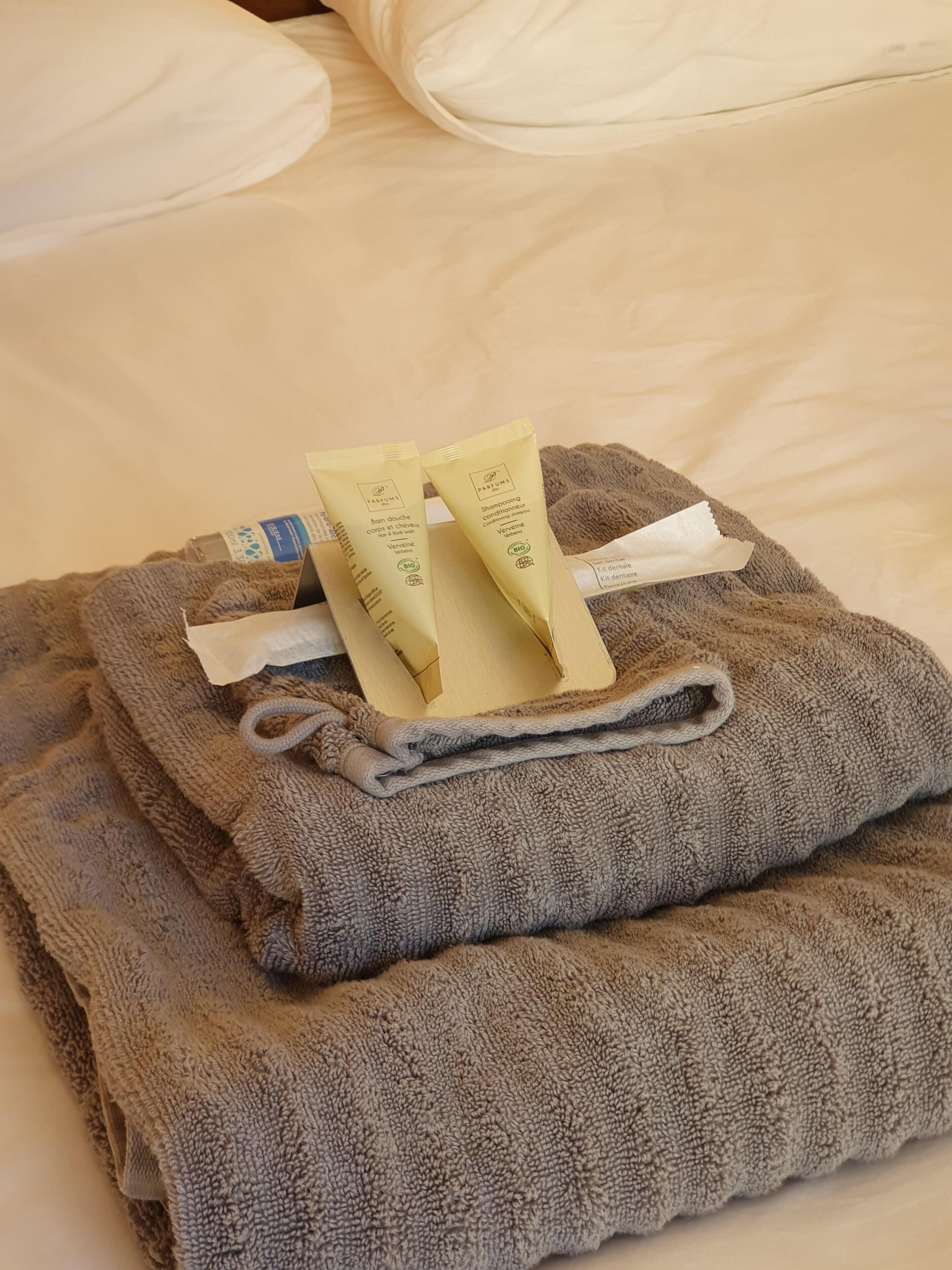 Een netjes opgevouwen grijze handdoek op een bed met een wit kussen.