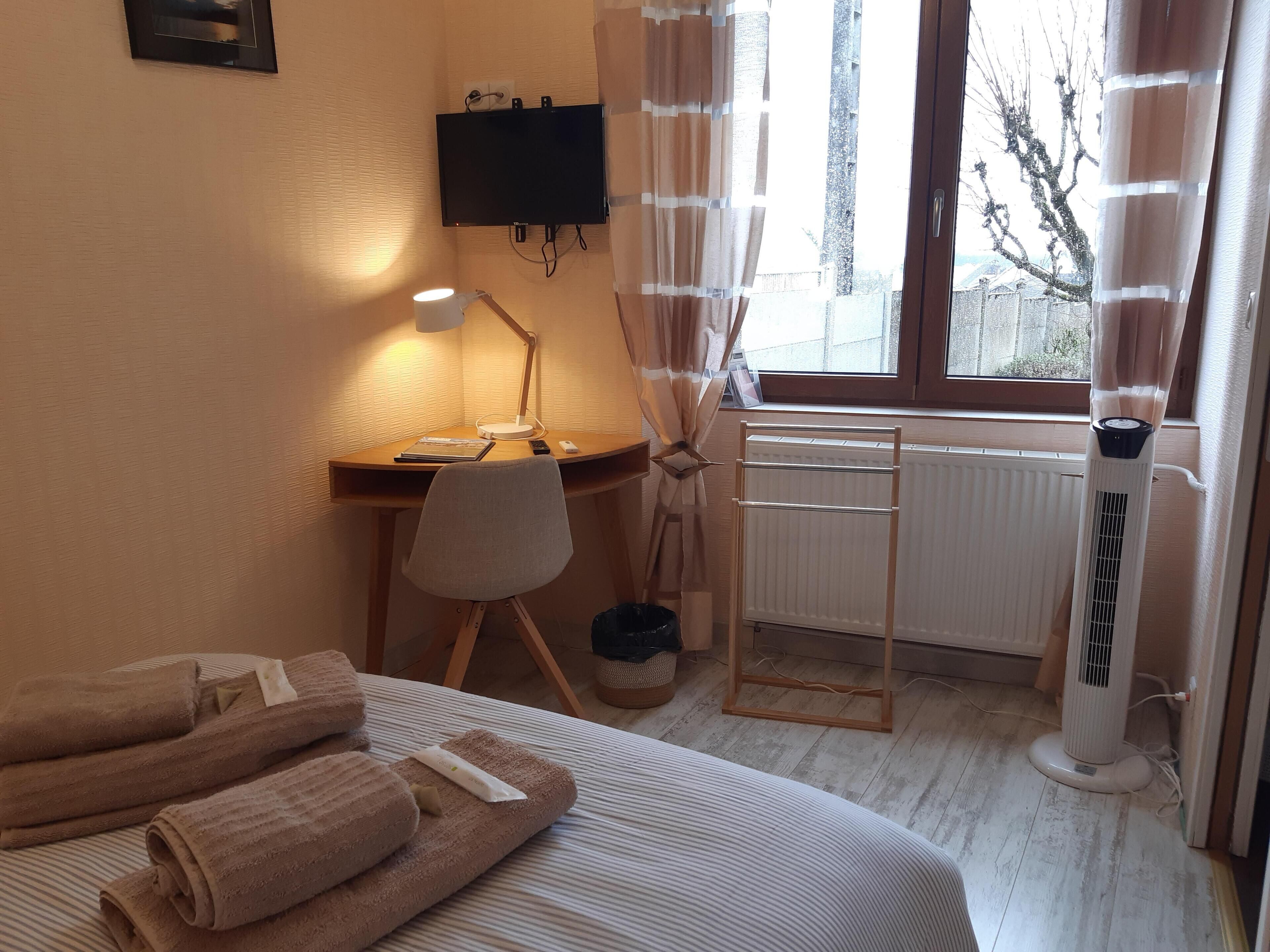 Habitación de hotel con cama, escritorio con lámpara, radiador y ventana con cortinas.