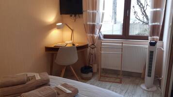 Habitación de hotel con cama, escritorio con lámpara, radiador y ventana con cortinas.