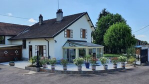 A two-story house with a conservatory, surrounded by potted plants and a gravel driveway. - Au Bon Vivant (Dampierre-sur-Salon)
