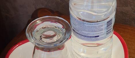 A clear glass bottle with a white cap and a glass lid on a white plate with red trim. The plate has a logo and text that reads "Moulin d'Horloge fondée en 1930".