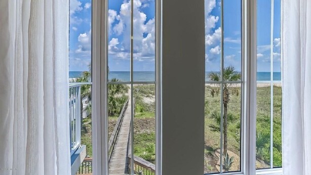 A room with large windows offering a view of a beach and a wooden boardwalk.