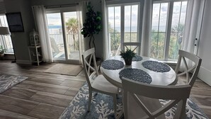A dining area with a table and chairs, a potted plant, and a view of the sea through large windows.