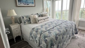 A bedroom with a bed, a nightstand, a ceiling fan, and a window with curtains.
