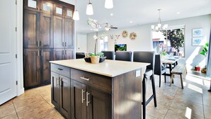 Une cuisine moderne avec des meubles de couleur bois foncé, un îlot central, des luminaires suspendus et un coin repas comprenant des chaises et une table.