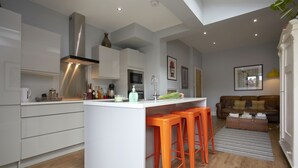 Cocina moderna con armarios blancos, extractor de acero inoxidable y una isla central con taburetes naranja.