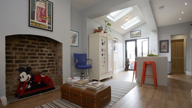 Una sala de estar con chimenea, un sillón azul, un armario blanco y un taburete rojo.