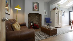 Una sala de estar con un sofá de cuero marrón, una lámpara de pie amarilla, una chimenea y un aparador con objetos decorativos.