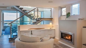 Un interior moderno con chimenea, un sofá y una escalera que conduce a un espacio exterior.