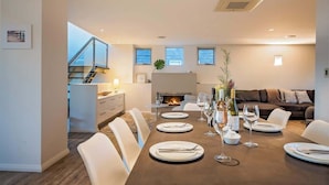 Un comedor moderno con una larga mesa dispuesta para seis personas, una chimenea y vistas al salón.