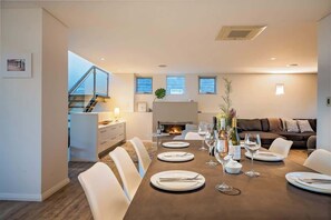 A modern dining room with a long table set for six, a fireplace, and a view of the living area.