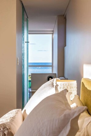 A hotel room with a bed, a small table, a window with a view of the sea, and a door leading to another room. - Shore House: Expansive Stunner by the Beach (Dunsborough)