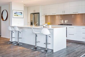 A modern kitchen with white cabinetry, a stainless steel refrigerator, a gas stove, and three bar stools. - Shore House: Expansive Stunner by the Beach (Dunsborough)
