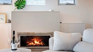 Una sala de estar moderna con chimenea, un sofá, una mesa redonda con una botella y vasos, y un reloj en la pared.