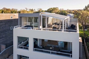 Un edificio moderno de dos pisos con balcón, ventanas grandes y mobiliario para exterior.