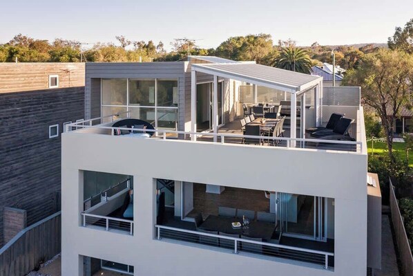 A modern two-story building with a balcony, large windows, and outdoor seating.