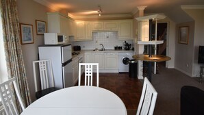 Cocina compacta con armarios blancos, microondas, lavamanos y comedor con mesa y sillas.