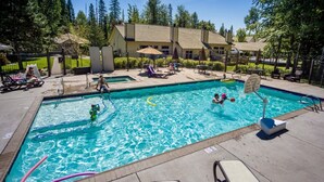 A swimming pool with clear blue water, surrounded by lounge chairs and umbrellas, with a house in the background.