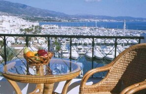 A balcony with wicker furniture, a glass table, and a fruit basket.